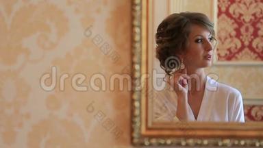 新娘穿着丝绸长袍，看着镜子，在结婚当天早上试穿她的结婚耳环